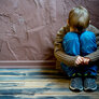 Bildet viser et lite barn som sitter mot en vegg med opptrukne knær og skjuler ansiktet sitt.