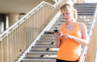 Bildet viser en ung kvinne med høretelefoner som ser på en telefon