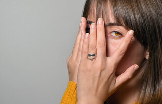 Bildet viser en kvinne med hendene foran øynen, men som titter mellom to fingre