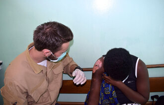Bildet viser en sykepleierstudent på utveksling i Afrika som steller et stort sår på skulderen til en ung dame