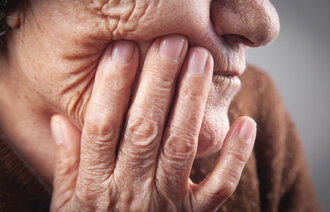 Bildet viser en eldre kvinne som tar seg til ansiktet ved munnen