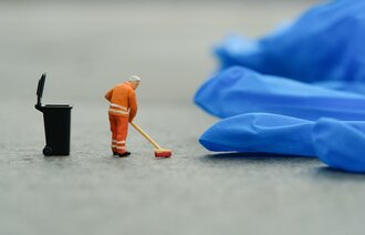 Bildet viser en miniatyrmann som koster opp rundt en engangshanske av plast