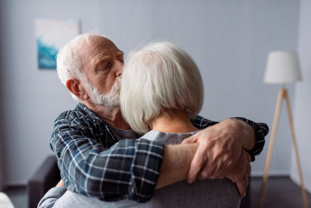 Bildet viser en eldre mann som omfavner en eldre kvinne mens han kysser henne på pannen.