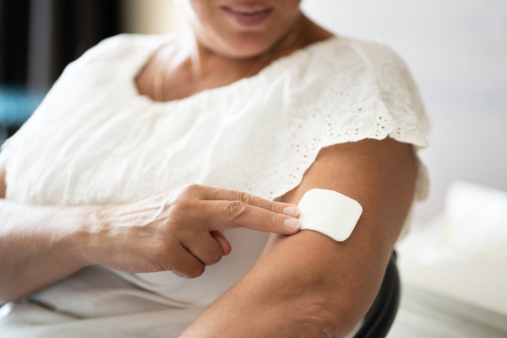 Bildet viser en kvinne som setter på et østrogen-plaster på overarmen.