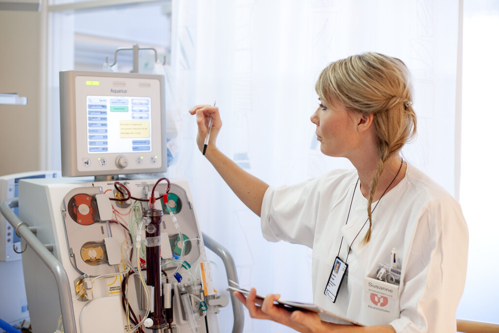 Bildet viser en intensivsykepleier som trykker på en skjerm på en maskin med masse slanger og annet utstyr