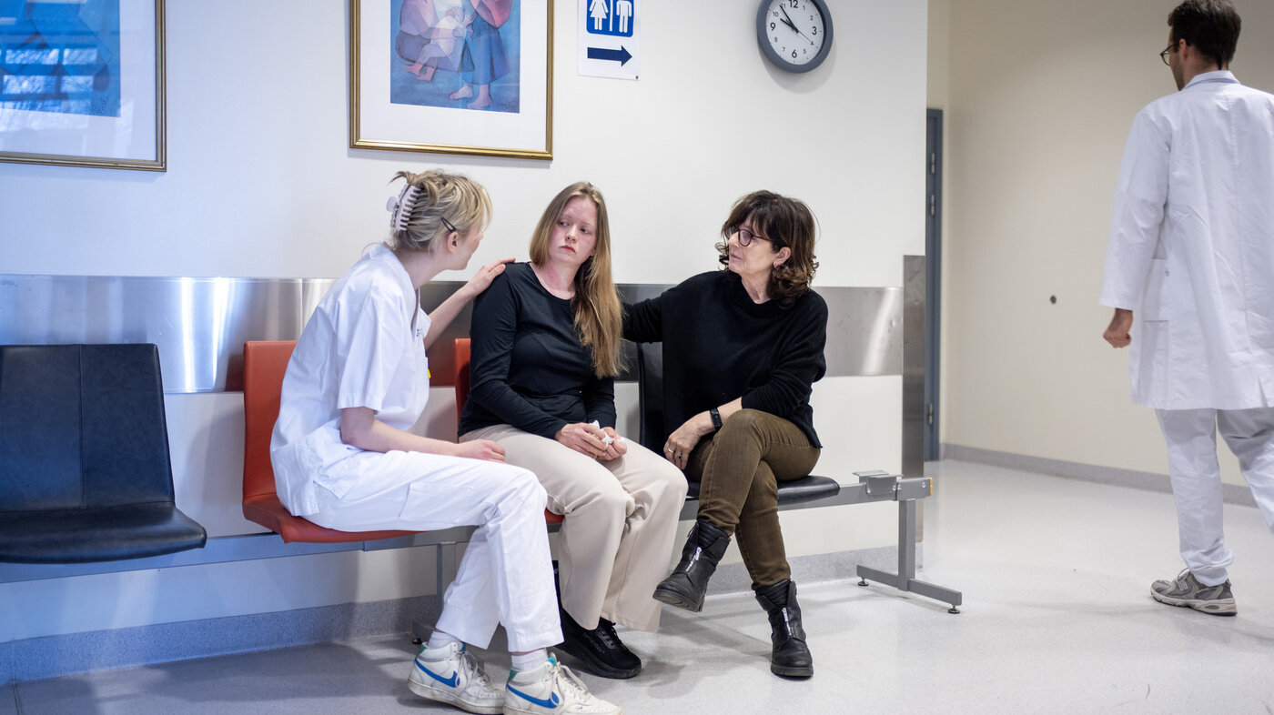 Bildet viser en ung kvinne som får trøst av pårørende og sykepleier på venteværelset. En lege går i bakgrunnen.