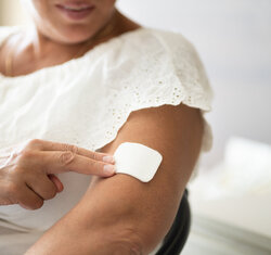 Bildet viser en kvinne som setter på et østrogen-plaster på overarmen.